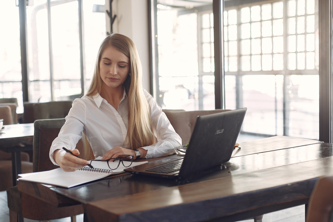 Young focused businesswoman working remotely with copybook in cafe during daytime